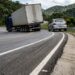 Caminhão e carro percorrem uma curva onde o pavimento sobe em direção ao lado externo.
