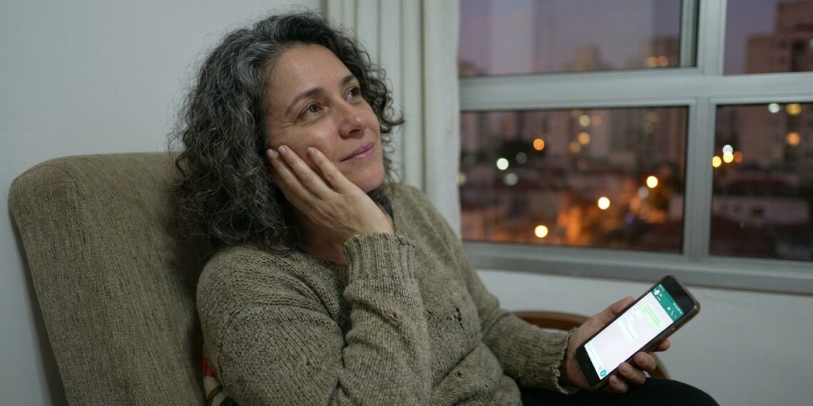 Mulher observa uma mensagem no celular e pensa antes de responder.