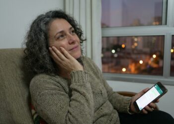 Mulher observa uma mensagem no celular e pensa antes de responder.