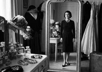 Coco Chanel diante do espelho em um ambiente luxuoso, usando um visual simples e elegante.