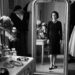 Coco Chanel diante do espelho em um ambiente luxuoso, usando um visual simples e elegante.