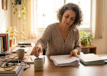 Mulher organiza papéis e objetos sobre a mesa de trabalho.