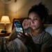 Mulher cansada continua rolando o celular na cama perto da meia-noite em vez de dormir.