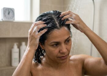 Mulher aplica shampoo anticaspa diretamente no couro cabeludo e mantém a espuma na raiz antes do enxágue.
