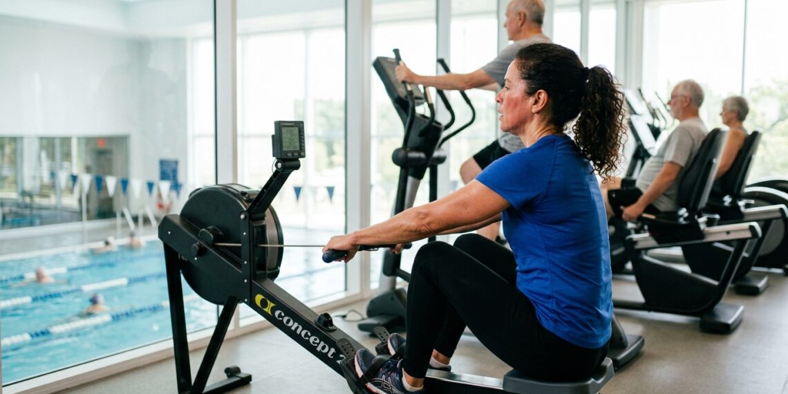 Mulher com mais de 50 anos faz exercício aeróbio no remo ergométrico em academia.