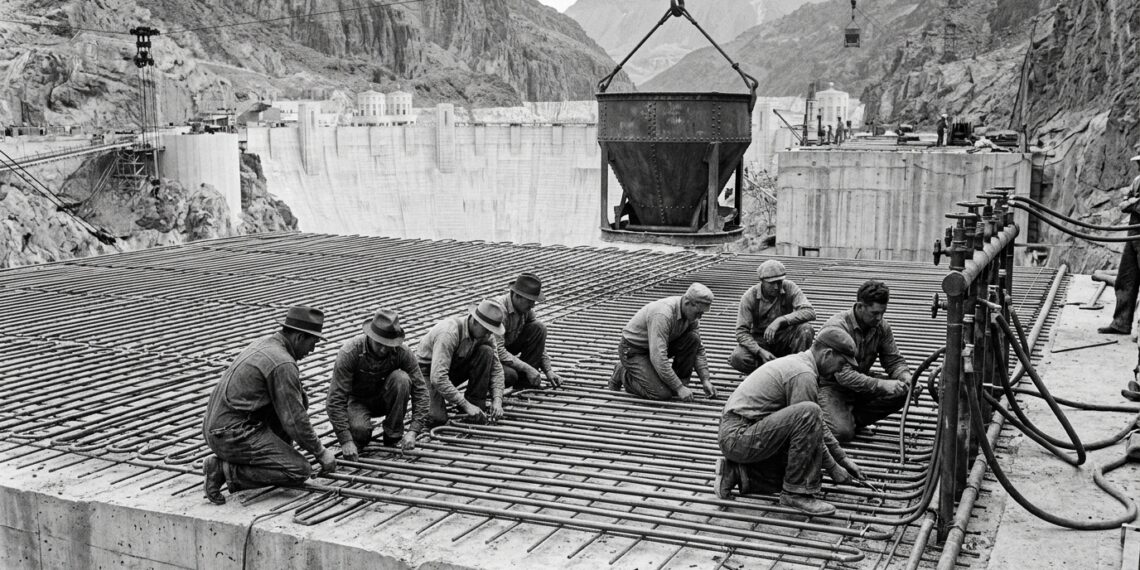 Trabalhadores instalam tubos de aço sobre uma camada de concreto durante a construção da Hoover Dam.