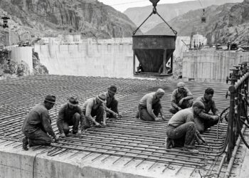 Trabalhadores instalam tubos de aço sobre uma camada de concreto durante a construção da Hoover Dam.