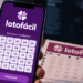 Lotofácil aparece na tela de celular enquanto rosto de inteligência artificial surge ao fundo.