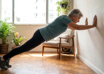 Pessoa com mais de 60 anos realiza flexão na parede em casa com postura controlada.