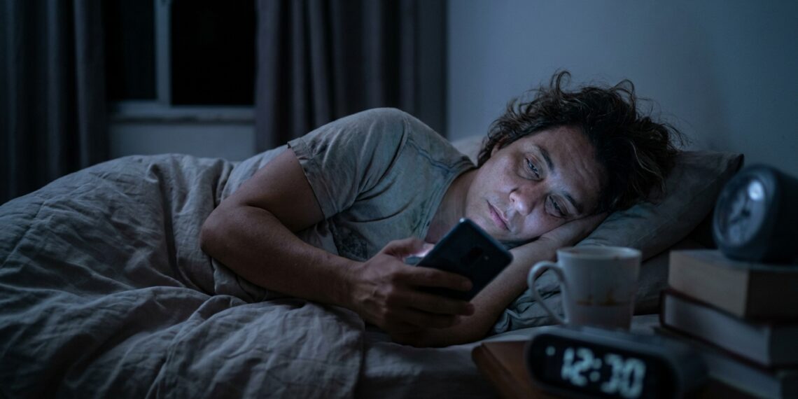 Pessoa cansada continua usando o celular na cama mesmo depois do horário em que pretendia dormir.