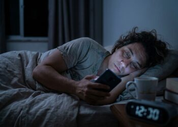 Pessoa cansada continua usando o celular na cama mesmo depois do horário em que pretendia dormir.