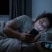 Pessoa cansada continua usando o celular na cama mesmo depois do horário em que pretendia dormir.