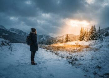 Pessoa diante de uma paisagem de inverno iluminada por raios dourados de sol, simbolizando esperança e força interior.