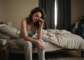 Pessoa acorda cansada e senta na cama após uma noite inteira de sono.