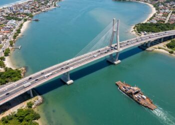 Ponte de Guaratuba cruza a baía enquanto uma balsa aparece ao fundo como referência à antiga travessia.