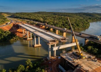 Vista aérea ilustrativa da nova ponte de concreto em construção sobre o Rio Jequitinhonha, ao lado da travessia antiga da BR-101, em Itapebi, Bahia.