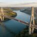 Vista aérea ilustrativa da Ponte da Integração sobre o Rio Paraná, mostrando duas torres de concreto, cabos de aço e o longo vão central entre Brasil e Paraguai.
