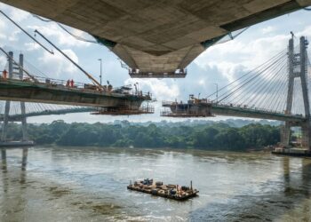 Vista próxima ao nível da água de uma representação da ponte estaiada sobre o Rio Xingu, com grande vão central, cabos inclinados e tabuleiro em construção.