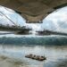 Vista próxima ao nível da água de uma representação da ponte estaiada sobre o Rio Xingu, com grande vão central, cabos inclinados e tabuleiro em construção.