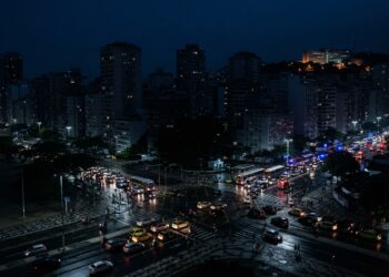 Cidade brasileira parcialmente às escuras durante um apagão, com trânsito e edifícios afetados pela falta de energia.