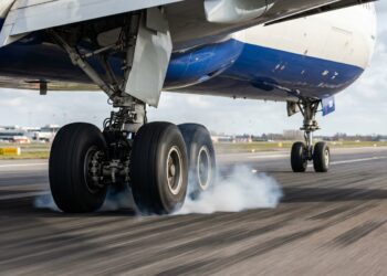 Pneus do trem de pouso de um avião comercial tocando a pista e liberando uma pequena nuvem de fumaça.