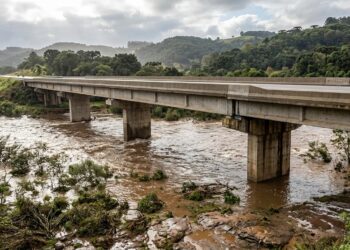 Ilustração de uma ponte rodoviária elevada de concreto sobre um rio com nível de água alto após chuvas intensas no Rio Grande do Sul.