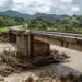 Ponte rodoviária de concreto sobre um rio na Serra Gaúcha, com troncos acumulados perto de um pilar.
