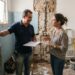 Profissional da construção mede um banheiro em reforma enquanto conversa com o proprietário sobre os serviços.