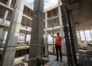 Engenheiro inspeciona as armaduras de aço instaladas nos pilares de concreto de um edifício alto em construção.