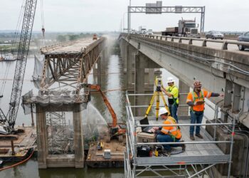 Sensores e equipes técnicas acompanham a ponte em operação enquanto a estrutura antiga é desmontada ao lado.