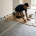 Instalador posiciona manta acústica sobre contrapiso nivelado antes de colocar o piso.