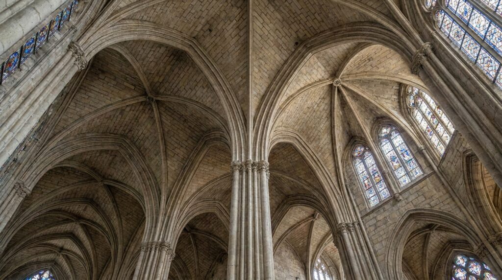Abóbadas de nervuras e arcos ogivais de pedra no interior de uma catedral gótica.