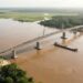 Ilustração conceitual de uma ponte rodoviária de 1.220 metros atravessando o Rio Mamoré entre Brasil e Bolívia, com vegetação amazônica nas margens.