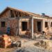 Casa térrea em construção com paredes de tijolos, estrutura de concreto e materiais de obra.