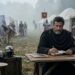 Marco Aurélio escreve em silêncio enquanto um acampamento romano desperta ao fundo.