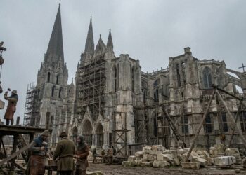 Catedral gótica medieval em construção, com torres de pedra, andaimes de madeira e trabalhadores medievais.