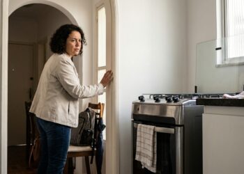 Pessoa olha novamente para o fogão desligado antes de sair de casa, demonstrando dúvida sobre uma ação já realizada.
