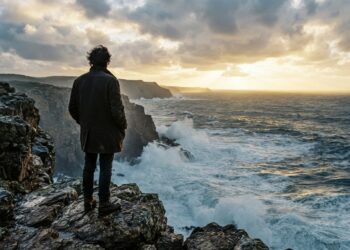 Pessoa contempla o oceano Atlântico de um miradouro rochoso ao amanhecer.