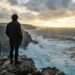 Pessoa contempla o oceano Atlântico de um miradouro rochoso ao amanhecer.