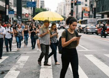 Pedestre concentrado no celular atravessa uma rua movimentada enquanto outros acontecimentos ocorrem ao redor.