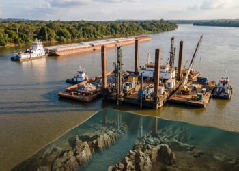 Plataforma perfura rochas submersas no Rio Tocantins enquanto grande comboio aguarda passagem.