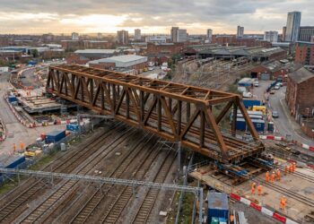 Vista aérea de uma enorme ponte metálica de treliça sendo deslocada lateralmente sobre uma ferrovia em Birmingham, na Inglaterra.