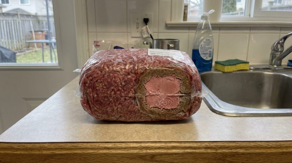 Carne parcialmente descongelada deixada sobre uma bancada de cozinha ao lado da pia.
