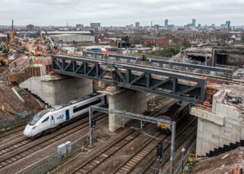 Nova ponte metálica elevada sobre linhas ferroviárias em Saltley, Birmingham, com trem elétrico passando sob a estrutura.