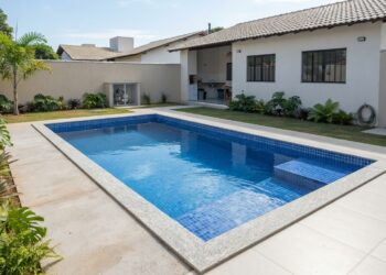 Piscina retangular de alvenaria com revestimento azul e bordas de pedra em um quintal residencial.