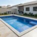 Piscina retangular de alvenaria com revestimento azul e bordas de pedra em um quintal residencial.