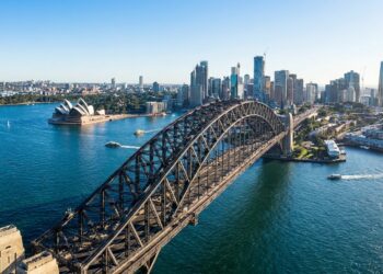 Sydney Harbour Bridge atravessa o porto de Sydney com a Ópera de Sydney e a cidade ao fundo.