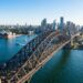 Sydney Harbour Bridge atravessa o porto de Sydney com a Ópera de Sydney e a cidade ao fundo.
