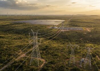 Torres de transmissão de energia elétrica atravessando o Cerrado brasileiro, com parques eólicos e solares ao fundo.