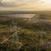 Torres de transmissão de energia elétrica atravessando o Cerrado brasileiro, com parques eólicos e solares ao fundo.